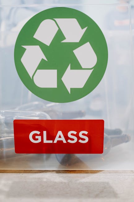 A clear glass door featuring a large green recycling symbol consisting of three chasing arrows arranged in a triangular loop, positioned centrally and slightly towards the top. Below the symbol, there